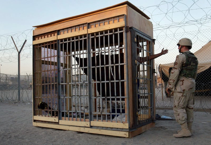 An inmate in an outdoor cell talks with a US military police officer at Abu Ghraib prison near Baghdad in June 2004. AP