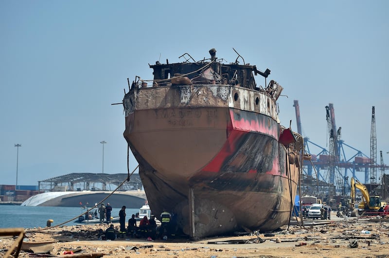Workers and members of Lebanese civil defence rest next to a damaged vessel. EPA