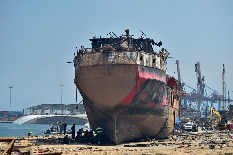 Workers and members of Lebanese civil defence rest next to a damaged vessel. EPA