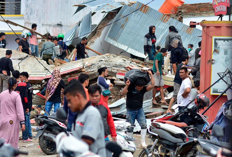 People retrieve goods from a collapsed convenience store as others are seen over building rubble in Mamuju city on January 16, 2021, a day after a 6.2-magnitude earthquake rocked Indonesia's Sulawesi island. AFP