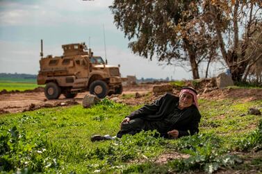 A man lies in a field near a US military vehicle on patrol along the M4 motorway near Hasakah in the countryside of Syria's northeastern province of Hasakah on April 3, 2020. / AFP / DELIL SOULEIMAN