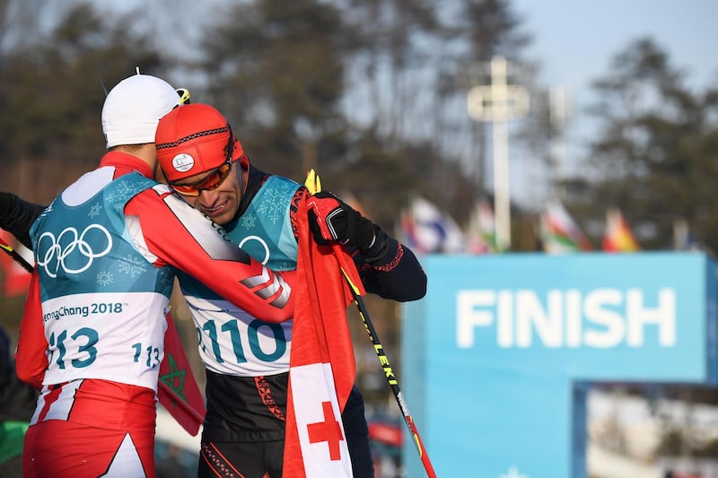 Morocco's Samir Azzimani (L) congratulates Tonga's Pita Taufatofua after he crossed the finish line during the men's 15km cross country freestyle at the Alpensia cross country ski centre during the Pyeongchang 2018 Winter Olympic Games on February 16, 2018 in Pyeongchang.  / AFP PHOTO / FRANCK FIFE