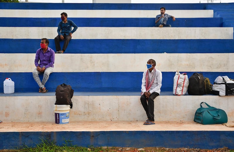 Migrant workers from Bihar state, wearing masks as a precaution against the coronavirus, watch local youth play football as they wait for buses to catch home bound train in Kochi, southern Kerala state, India. AP Photo