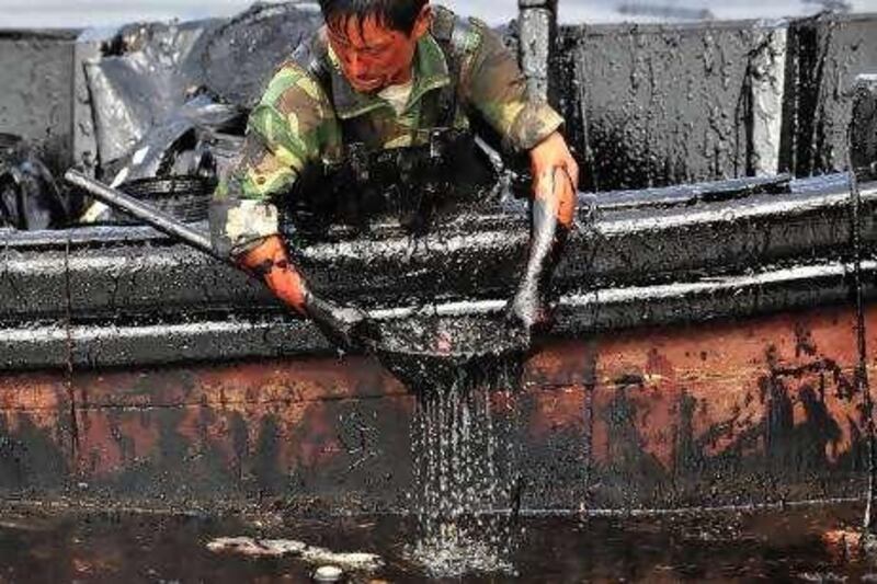 A worker scoops oil from the oil spill site near Dalian Port, Liaoning province July 26, 2010. Dalian Port has resumed operations at two of its oil berths and its main 300,000 tonnage berth is expected to reopen soon, the company said on Sunday, after a fire at the port a week ago shut the berths down. REUTERS/Stringer (CHINA - Tags: DISASTER ENERGY ENVIRONMENT) CHINA OUT. NO COMMERCIAL OR EDITORIAL SALES IN CHINA