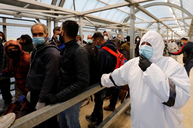 A health worker watches as Palestinian laborers head to work in Israel through a checkpoint amid concerns about the spread of the coronavirus disease (COVID-19), near Hebron in the Israeli-occupied West Bank May 3, 2020. REUTERS/Mussa Qawasma