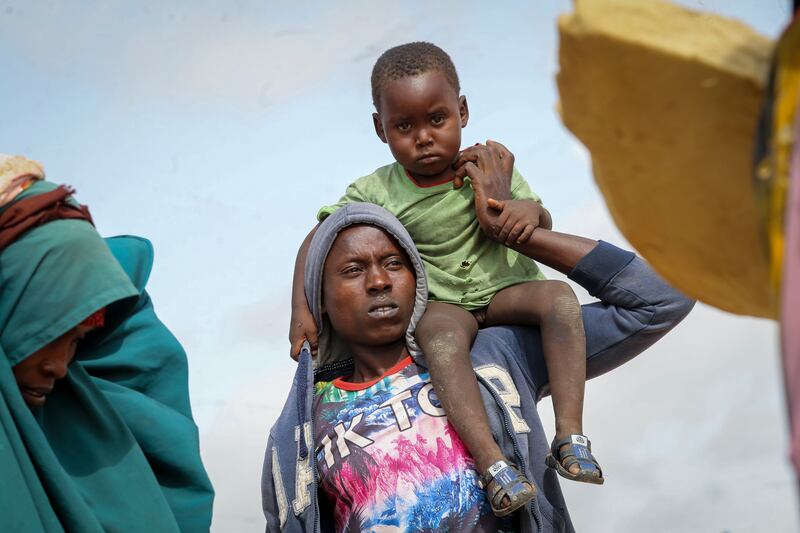 A man carries a child as he and others who fled drought-stricken areas arrive at a makeshift camp for the displaced, on the outskirts of Mogadishu, Somalia. AP