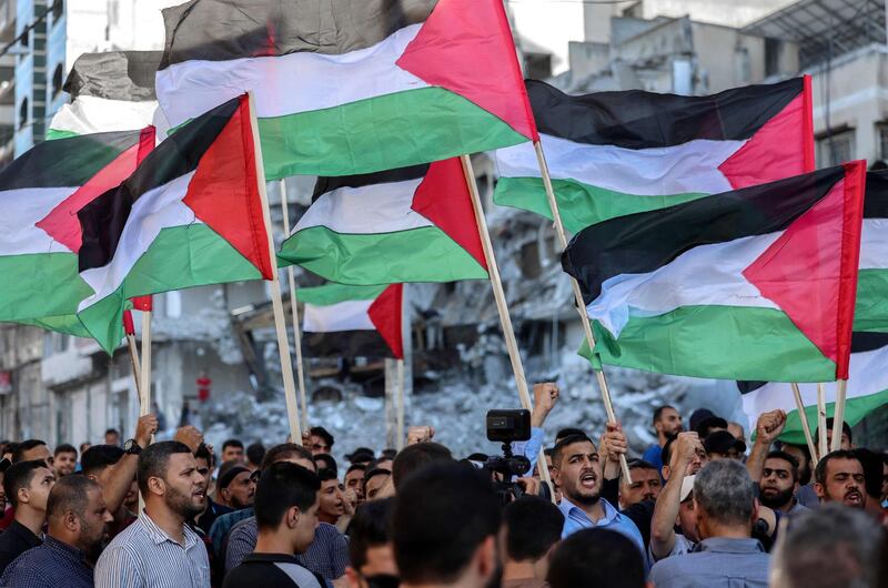 Palestinians lift national flags as they march past buildings destroyed by Israeli air strikes in Gaza City on June 15, 2021, during a protest over the Israeli ultranationalist March of the Flags in Jerusalem's Old City which celebrates the anniversary of Israel's 1967 occupation of Jerusalem's eastern sector. / AFP / MOHAMMED ABED
