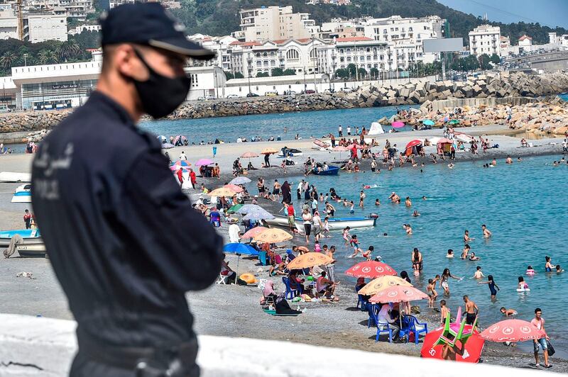 A policeman, mask-clad, watches as people cool off in the water at El Kettani beach in the Bab El Qued suburb of Algeria's capital Algiers as the country eases pandemic restrictions.  AFP