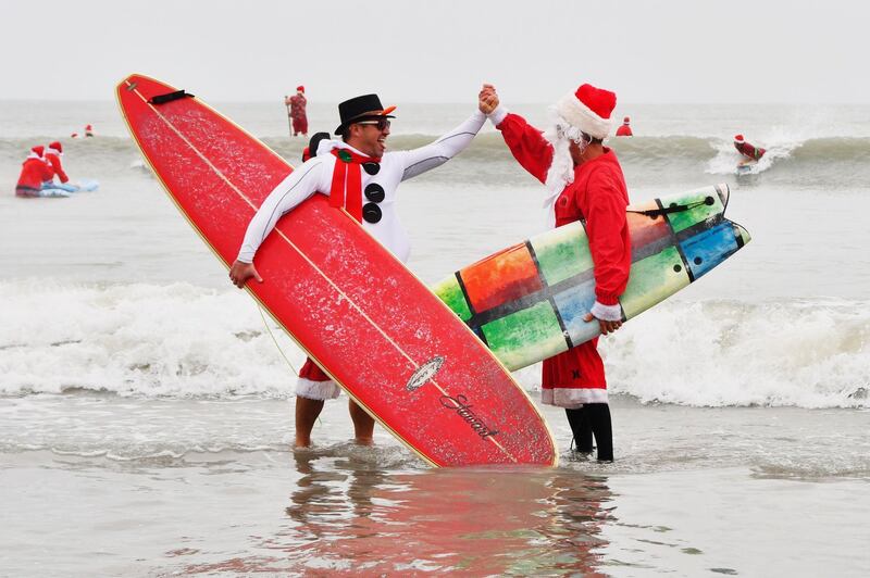 George Trosset Jr. and George Trosset, who started surfing in Christmas costumes ten years ago, high five each other during the 10th annual Surfing Santas event in Cocoa Beach, Flordia.  AP