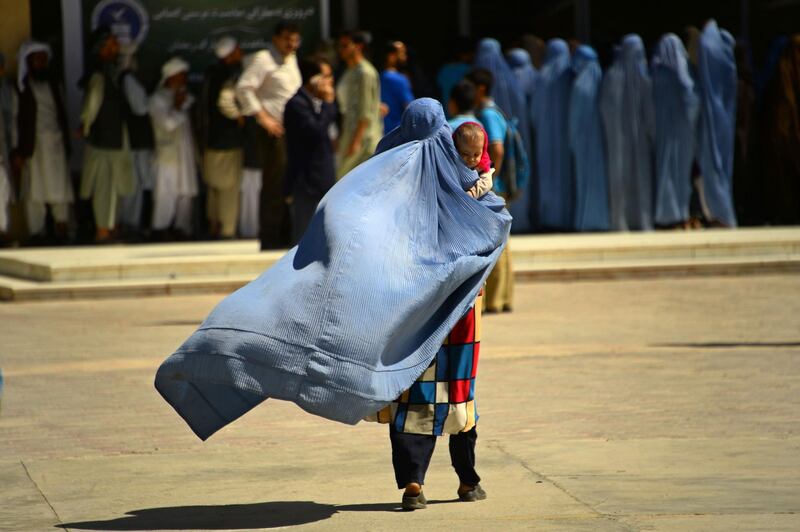 An Afghan woman walks a she holds a child before receiving aid by a charity during the holy month of Ramdan in Herat province. Hoshang Hashimi / AFP