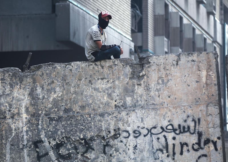 A masked Iraqi demonstrator sits atop of a concrete barrier as protesters gather in Tahrir Square. AFP