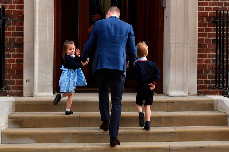 Princess Charlotte of Cambridge (L) turns to wave at the media as she is lead in with her brother Prince George of Cambridge (R) by their father Britain's Prince William, Duke of Cambridge, (C) at the Lindo Wing of St Mary's Hospital. (AFP / Ben STANSALL)