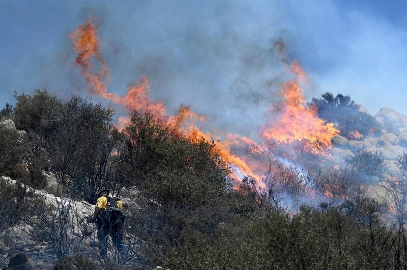 Flames from a brush fire flare around a firefighter in San Bernardino, California. James Quigg / The Daily Press via AP