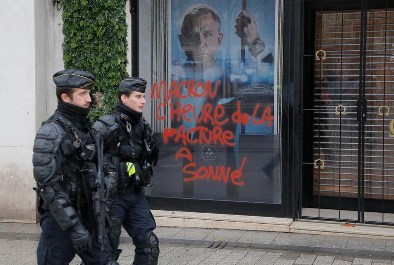 Police officers patrol at the Champs Elysees avenue in Paris, France, Sunday, Nov 25, 2018, in the aftermath of a protest against the rising of the fuel taxes. French President Emmanuel Macron has condemned violence by protesters at demonstrations against rising fuel taxes and his government. Tag on the shop window reads, "Macron it's time to pay the bill". (AP Photo/Michel Euler)