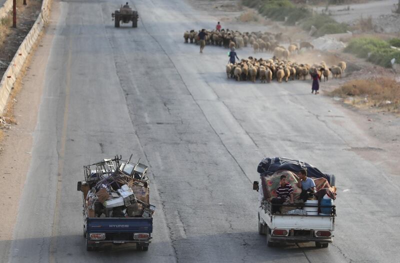 TOPSHOT - Syrian families from the southeastern Idlib province and the northern countryside of Hama fleeing battles with trucks loaded with their belongings, drive past a flock of sheep on the highway, as they drive near Maaret al-Numan in the southern Idlib province on August 14, 2019.   / AFP / Omar HAJ KADOUR
