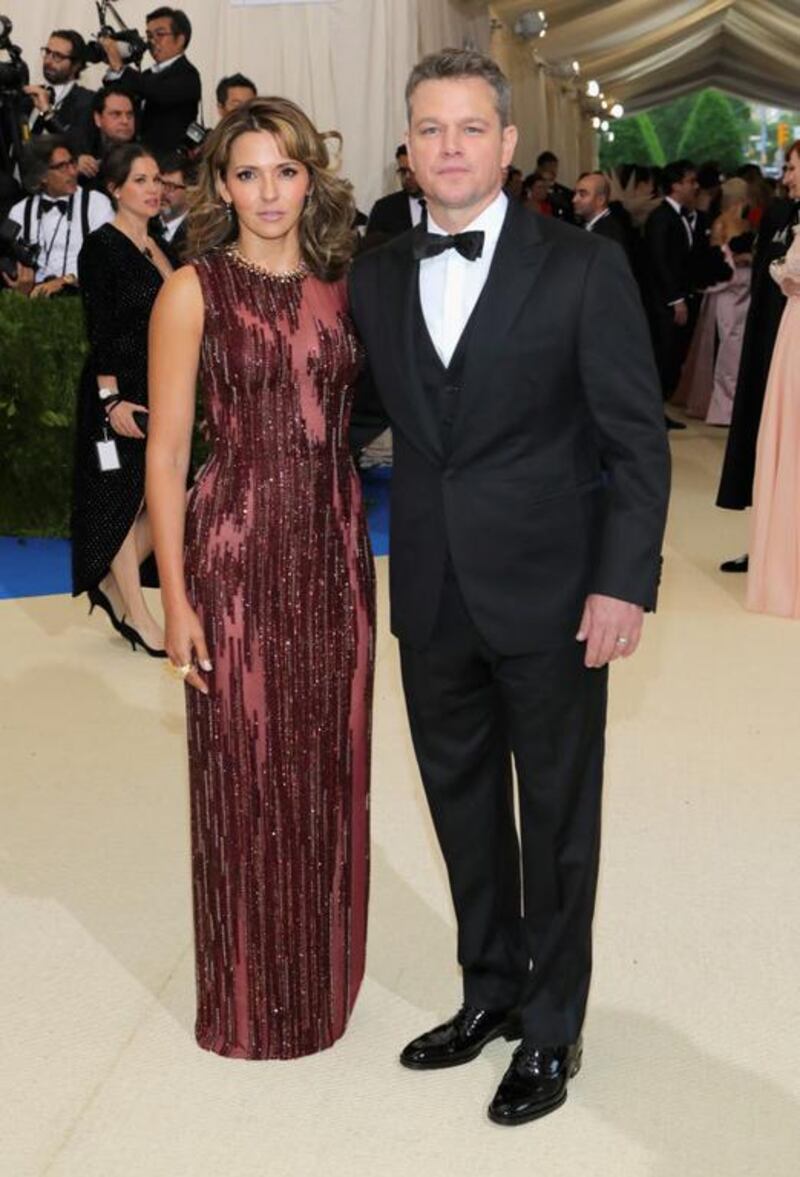 Luciana Barroso exudes elegance in a red Atelier Versace gown embellished with Swarovski crystal details, while husband Matt Damon complements her look in a three-piece Versace tuxedo. Courtesy of Versace
