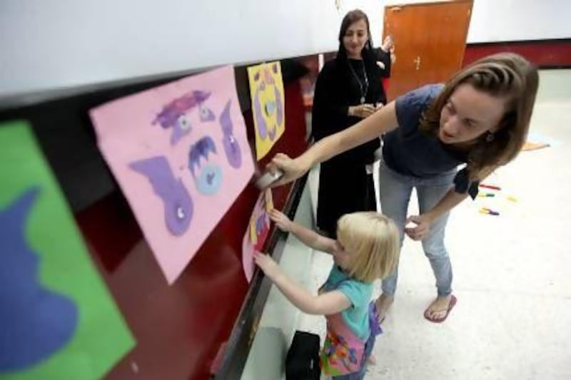 Pam Saulet, right, and Dana Shabaneh help Alice, 2, hang her artwork at St Andrews Church, Abu Dhabi, where Messy Monkeys hosts its art and craft sessions. Sammy Dallal / The National