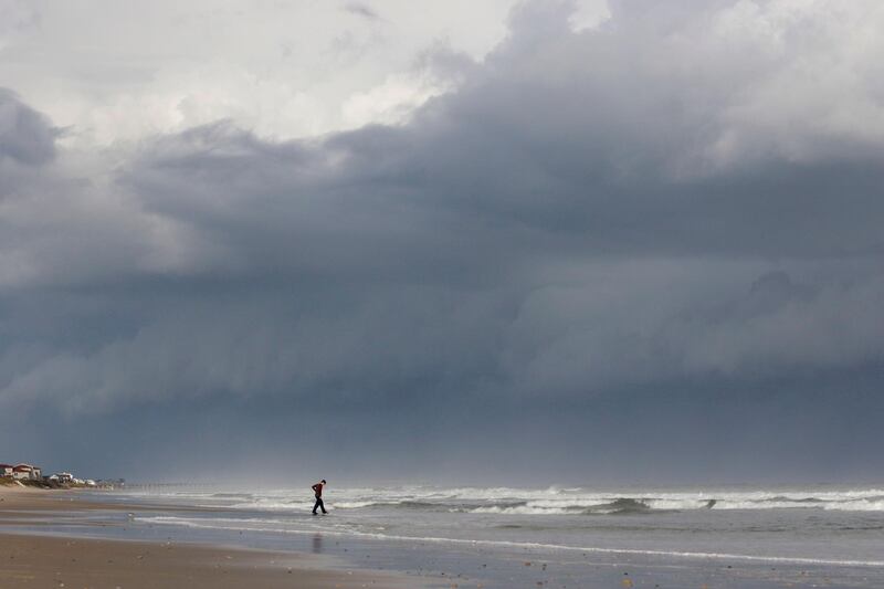 A storm front looms behind Seth Loconte as he walks on the beach in North Topsail Beach, North Carolina. AP Photo