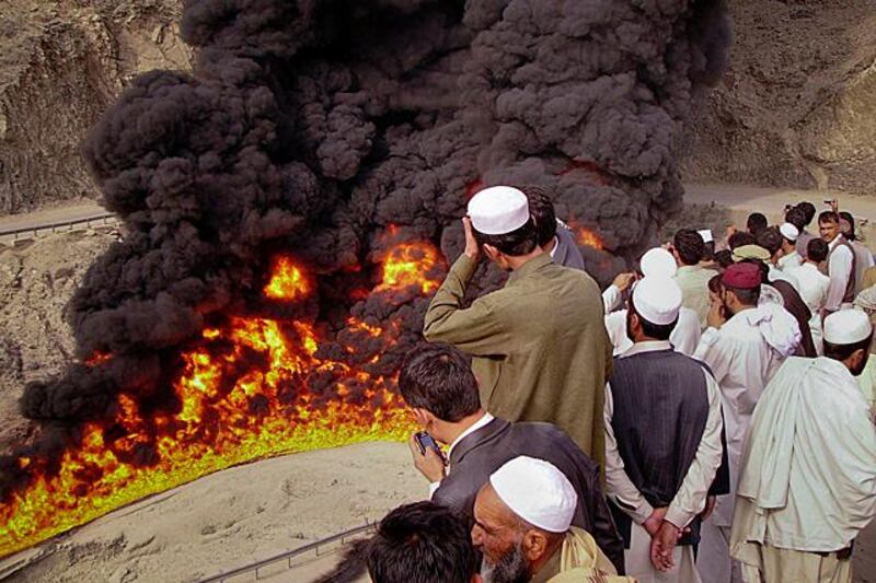 Passengers stand outside their vehicles to look at a burning oil tanker set ablaze by a bomb explosion after the road to the Afghan-Pakistan border was temporarily shut, on the outskirts of Landikotal November 23, 2011. The tanker, carrying fuel for Nato troops in Afghanistan, was attacked and set ablaze on Wednesday in the bomb blast, police said. No casualties were reported. REUTERS/Shahid Shinwari  (PAKISTAN - Tags: POLITICS CIVIL UNREST CRIME LAW TRANSPORT TPX IMAGES OF THE DAY MILITARY)