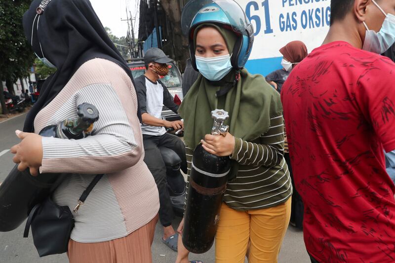 A woman carries her oxygen tank after having it refilled at a recharging station in Jakarta, Indonesia.
