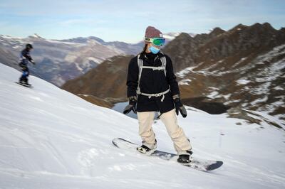 A snowboarder wearing a protective face mask aagainst the spread of the Covid-19 (novel coronavirus), boards down the slopes above the Swiss ski resort of Verbier in the Swiss Alps on November 15, 2020. - The coronavirus crisis shuttered Switzerland's ski resorts in the spring, but they are banking on tighter precautions and the Swiss love of the mountains to save them as the winter season begins. (Photo by Fabrice COFFRINI / AFP)