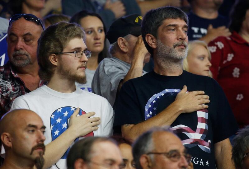 Men wearing QAnon movement shirts, stand for the Star-Spangled Banner, the national anthem of the United States, at the start of U.S. President Donald Trump's Make America Great Again rally at the Civic Center in Charleston, West Virginia, U.S., August 21, 2018.    REUTERS/Leah Millis