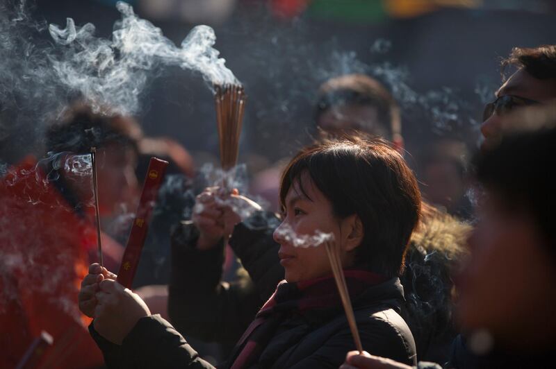 A woman burns incense at the Lama Temple in Beijing. Mark Schiefelbein / AP Photo