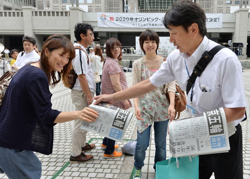 A vendor (R) hands out extra editions of a newspaper to people gathering at the Tokyo metropolitan government building, reporting on Tokyo's winning bid to be the host city of the 2020 Olympics on September 8, 2013. Tokyo won the right to host the Olympic Games for the second time, overcoming fears about radiation from the stricken Fukushima nuclear plant to land the 2020 edition of the world's biggest sporting event.   AFP PHOTO / KAZUHIRO NOGI
 *** Local Caption ***  894444-01-08.jpg