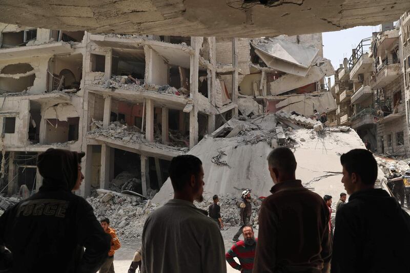 TOPSHOT - People watch as members of the Syrian Civil Defence, also known as the "White Helmets", search the rubble of a collapsed building following an explosion in the town of Jisr al-Shughur, in the west of the mostly rebel-held Syrian province of Idlib, on April 24, 2019. Over a dozen people, all but two civilians, were killed in an explosion in the jihadist-held region of Idlib in northwest Syria on Wednesday, the Britain-based Syrian Observatory for Human Rights said. The cause of the blast was not immediately clear. Idlib province is under administrative control of Hayat Tahrir al-Sham, Syria's former Al-Qaeda affiliate, with the Turkestan Islamic Party, a group of foreign jihadists from the ethnic Uighur Muslim minority, also having a large presence in the town. / AFP / OMAR HAJ KADOUR
