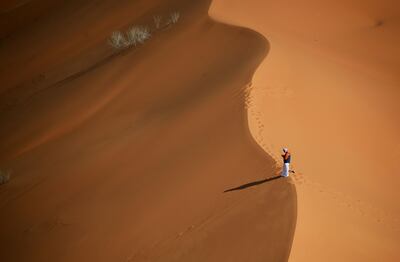 A man stands on top of a sand dune during the 6th Stage of the Dakar Rally 2021 between Buraydah and Hail, in Saudi Arabia, on January 8, 2021.  / AFP / FRANCK FIFE
