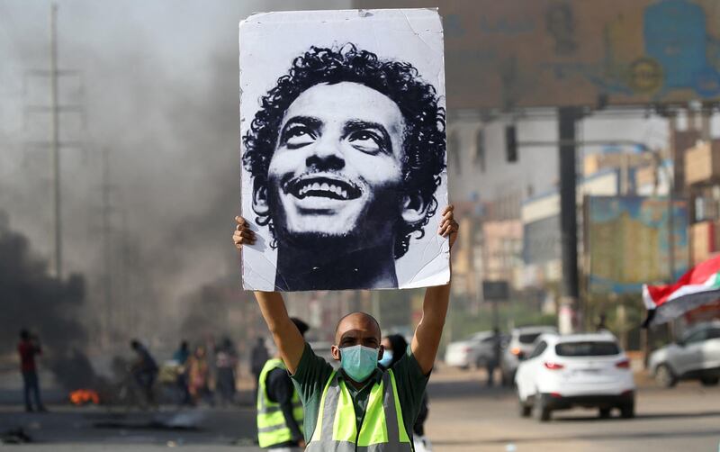 A mask-clad man holds a picture of a Abdulsalam Kisha, a Sudanese protester who was killed in a raid on an anti-government sit-in in 2019, during a protest in the Riyadh district in the east of the capital Khartoum on the anniversary of the raid on June 3, 2020. - One year after the 25-year-old Abdulsalam's killing in the dispersal of Sudan's main protest camp, his father Kisha is still holding out hope that the killers be brought to justice as he calls for an international probe. The young protester was killed along with scores others when armed men in military fatigues stormed the sprawling encampment outside Khartoum's army headquarters on June 3 last year. (Photo by ASHRAF SHAZLY / AFP)
