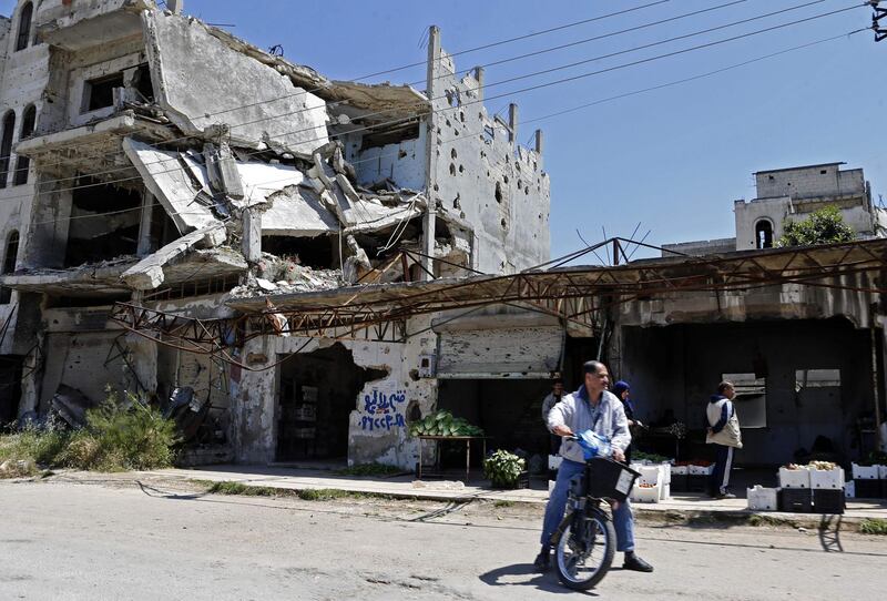 Syrians sell vegetables next to buildings heavily damaged during Syria's civil war, in the central city of Homs.  AFP