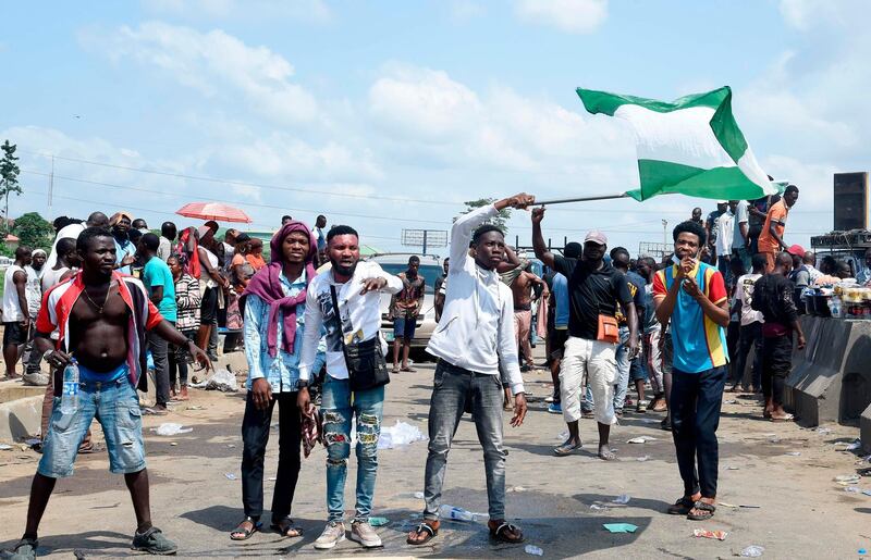 A protester waves a Nigerian national flag behind barricades mounted on the Lagos-Ibadan expressway to protest against police brutality and the killing of protesters by the military, at Magboro, Ogun State, on October 21, 2020.  Buildings in Nigeria's main city of Lagos were torched on October 21, 2020 and sporadic clashes erupted after the shooting of peaceful protesters in which Amnesty International said security forces had killed several people.
Witnesses said gunmen opened fire on a crowd of over 1,000 people on the evening of October 20, 2020, to disperse them after a curfew was imposed to end spiralling protests over police brutality and deep-rooted social grievances.  / AFP / PIUS UTOMI EKPEI
