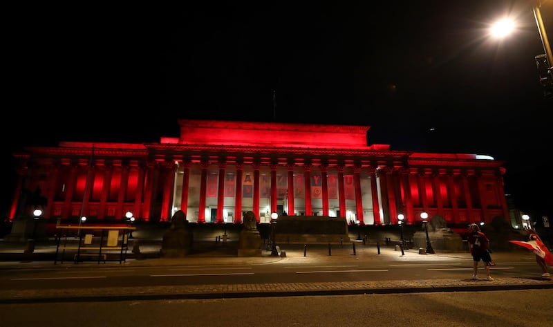 Liverpool fans celebrate outside St George's Hall which is lit up red. PA
