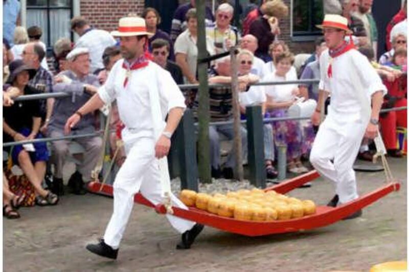 Tourists watch two traditionally dressed man carry a tray of cheese in Edam.