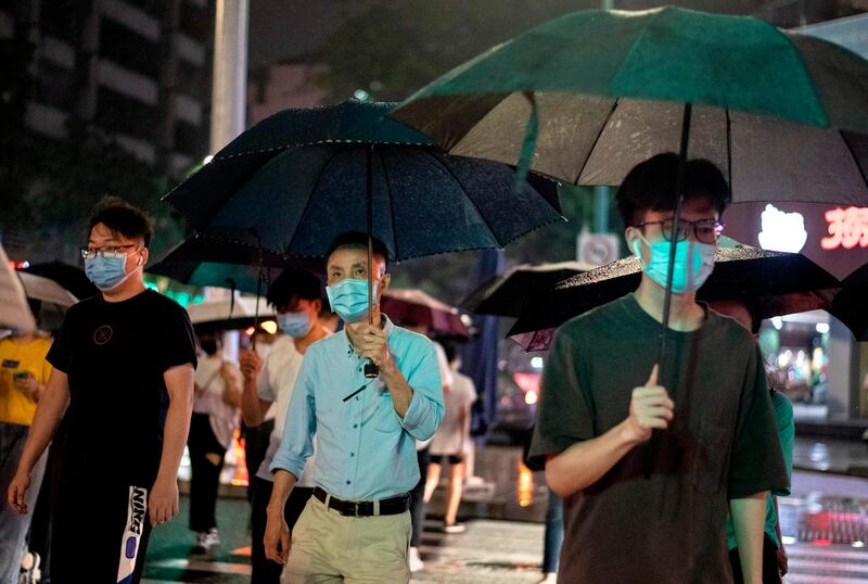 People wearing protective face mask walk under their umbrellas as it rains in Shenzhen in China's southern Guangdong province on May 22, 2020, as the nation moves slowly into normality following the novel coronavirus, COVID-19, pandemic.  / AFP / NOEL CELIS
