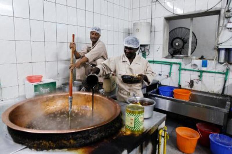 Al Ain, October 24, 2012 --  A staffing agency worker stirs a bubbling pot of halawa as another worker pours in black sugar to temper the mixtures in the kitchen at Zahran Al Harasi Omani Sweets shop in Al Ain, October 24, 2012. The black sugar imparts a bold, rich flavor and is used to make one of the more popular selling varieties of the sweet. (Photo by: Sarah Dea/The National)