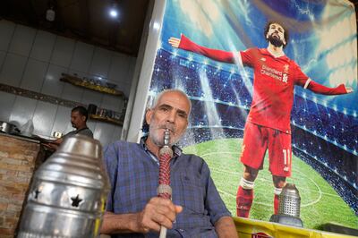 An Egyptian smokes a traditional water pipe while seated below an image of Liverpool's Mohamed Salah at a coffee shop in Cairo. AP