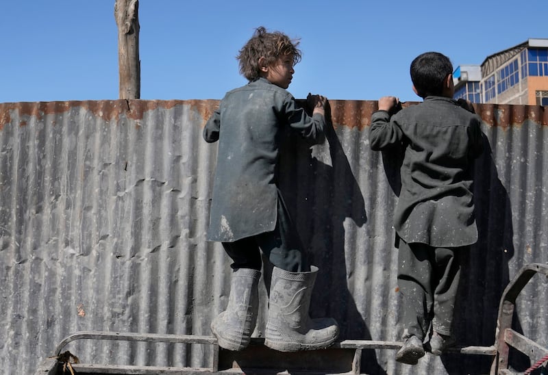 Afghan boys watch over a fence as aid agencies distribute food to people in need in Afghanistan's capital Kabul. AP