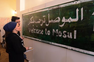 Visitors stand in front of a 'Welcome to Mosul' road sign displayed on January 29, 2019 at an art hall in the museum of the northern Iraqi city of Mosul, which served as the Islamic State (IS) group's brutal seat of power for three years, before Iraqi troops recaptured it in 2017. Mosul's celebrated museum has not recovered since IS jihadists ravaged its ancient treasures several years ago, but part of the complex reopened today to showcase more modern art.AFP