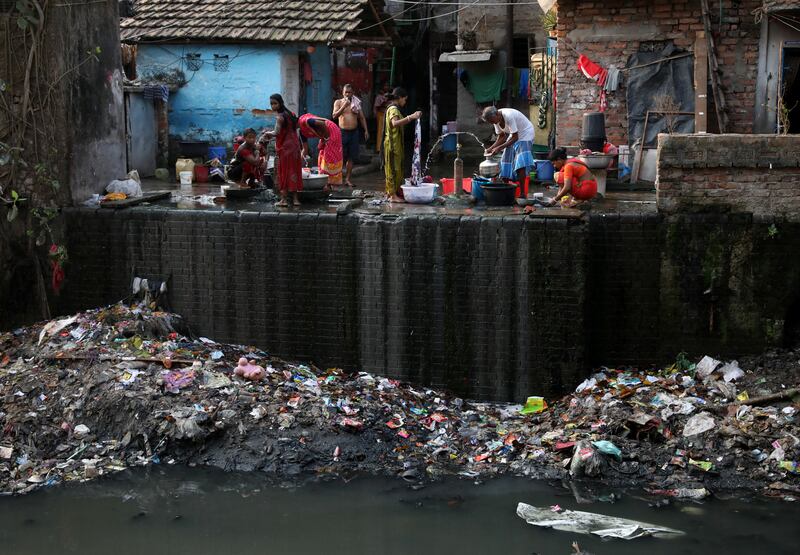 Residents fill water containers and wash their clothes from municipal water pipes alongside a polluted water channel at a slum in Kolkata, India. Reuters