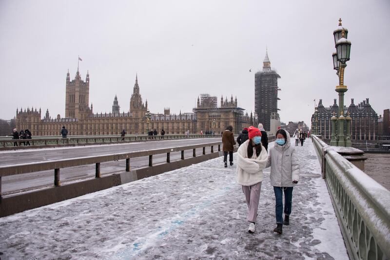 People wear face masks as they walk on Westminster Bridge against the backdrop of the Palace of Westminster, during a snowfall in London. Conditions are set to become more hazardous going into the final week of January with weather warnings for snow and ice. AP Photo