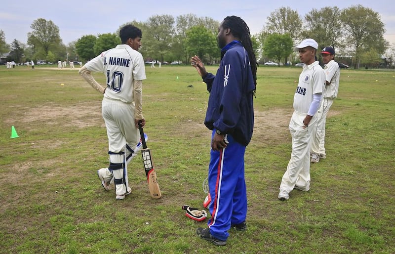 In this May 12, 2014 photo, Linden Fraser, second from left, New York regional cricket head coach, chats with John Adams High School player Derick Narine, left, before he bats in a match against Midwood High School . Fraser, also a coach for the US women's national cricket team, often makes the rounds to high school matches to offer advice and support. Bebeto Matthews / AP