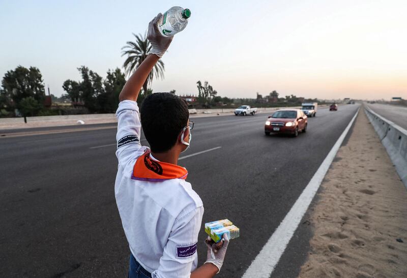A boyscout volunteering to distribute water, food and juice, signals to fasting drivers on a road in Egypt's Menoufia governorate on April 27, 2020, during the Muslim holy month of Ramadan. (Photo by Mohamed el-Shahed / AFP)