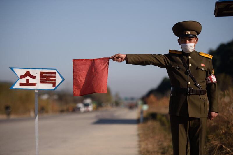 In this photo taken on October 29, 2020, a public security officer uses a red flag to stop a taxi for disinfection as part of preventative measures against the COVID-19 coronavirus, on a road at the entrance to Wonsan, Kangwon Province. (Photo by KIM Won Jin / AFP)