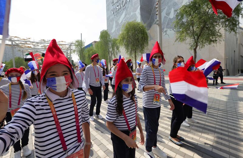 A group of French people wearing traditional berets, Phrygian caps and mariniere shirts, wave national flags as they parade during the Expo 2020. AFP
