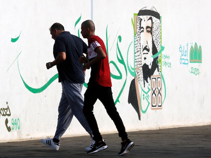 People jog in a public park past wall art showing Saudi's King Salman in Jeddah. AP Photo