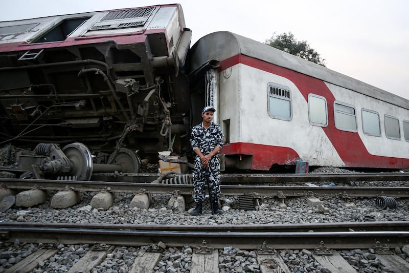 A member of Egyptian security forces stands guard before an overturned passenger carriage at the scene of a railway accident in the city of Toukh in Egypt's central Nile Delta province of Qalyubiya on April 18, 2021. - The train accident north of Cairo on April 18 left 11 people dead and 98 others injured, after it derailed off its tracks heading northwards from the capital Cairo, the health ministry said, in the latest railway disaster. Eight carriages derailed off the tracks as the train headed to Mansoura, about 130 kilometres north of Cairo. (Photo by Ayman Aref / AFP)