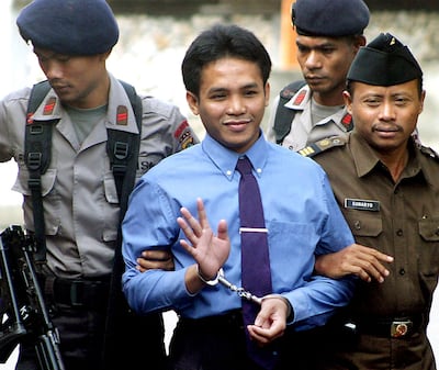 Ali Imron waves to photographers while police escort him into the courtroom in Denpasar, Indonesia, during his trial. AFP 