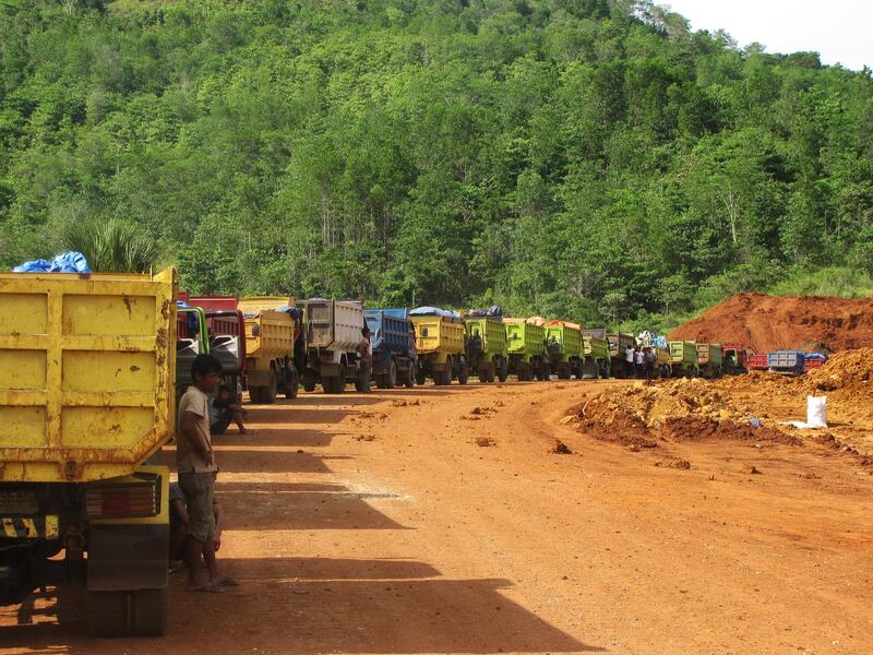 A March 2012 photo of a fleet of trucks queuing near a nickel laterite mine outside Kendari, Southeast Sulawesi province, Indonesia.  The nickel rich soil has formed over nickel-bearing ultramafic rocks.  An upper layer of red-brown material also contains cobalt in what geologists call limonite.  Below the limonite is the more yellowy saprolite horizon which contains higher grades of nickel, sometimes in excess of 2% nickel.  Trucks take the nickel ore from the mining area along a haul road to nearby stockpiles.